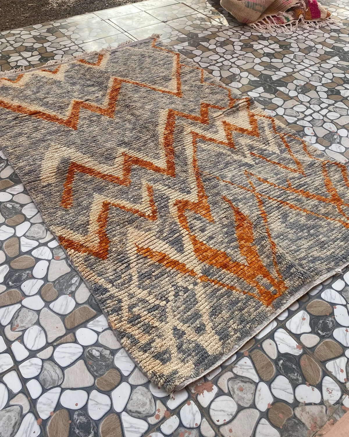 Gray and Orange Zigzag Moroccan Rug, seen at an angle on the workshop floor