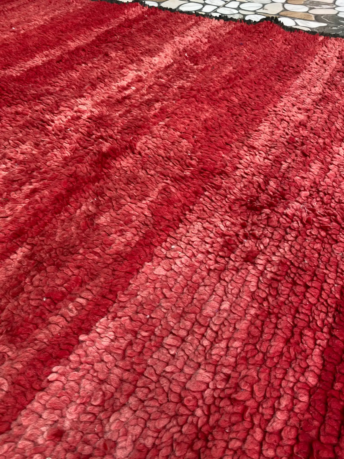 Close-up of the red rug's thick looped pile showing lighter and darker tonal stripes running across the surface