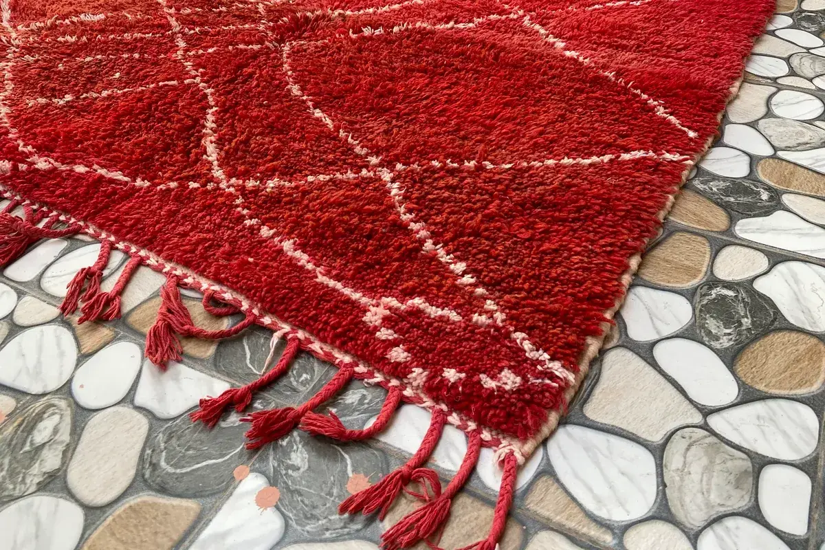 Corner of a red Beni Ourain rug with an ivory lattice and red fringe on a tiled floor
