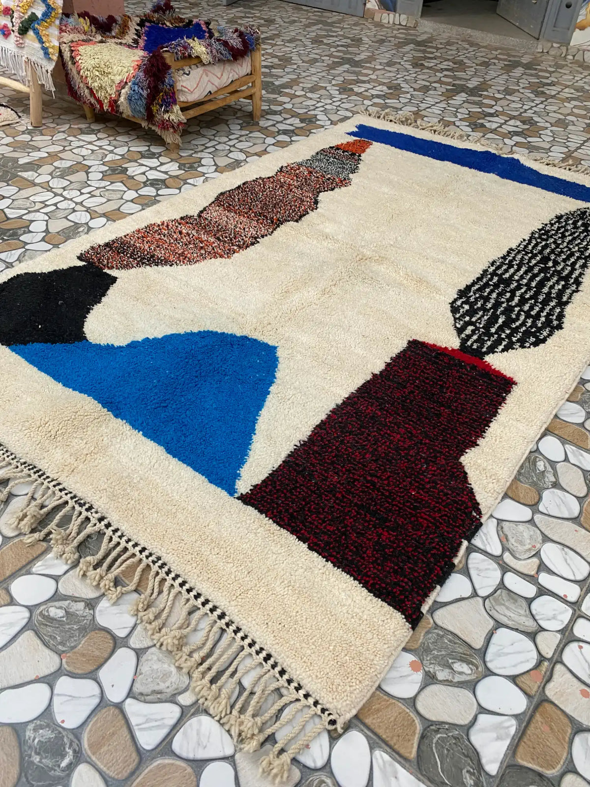 Rug laid on a pebble-patterned tile floor, angled to show the blue triangle and burgundy block