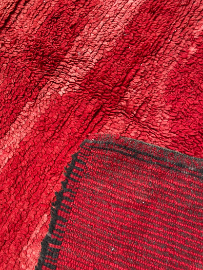 Close-up of the red shaggy pile with lighter pink stripes and a folded corner showing the flat-woven striped back
